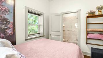 A bedroom with a bed, a window, a door, and a shelf with towels.