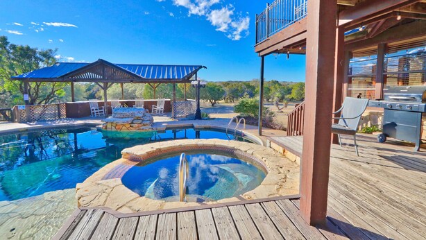 Un espace piscine comprenant un jacuzzi, une terrasse en bois et des sièges d’extérieur.