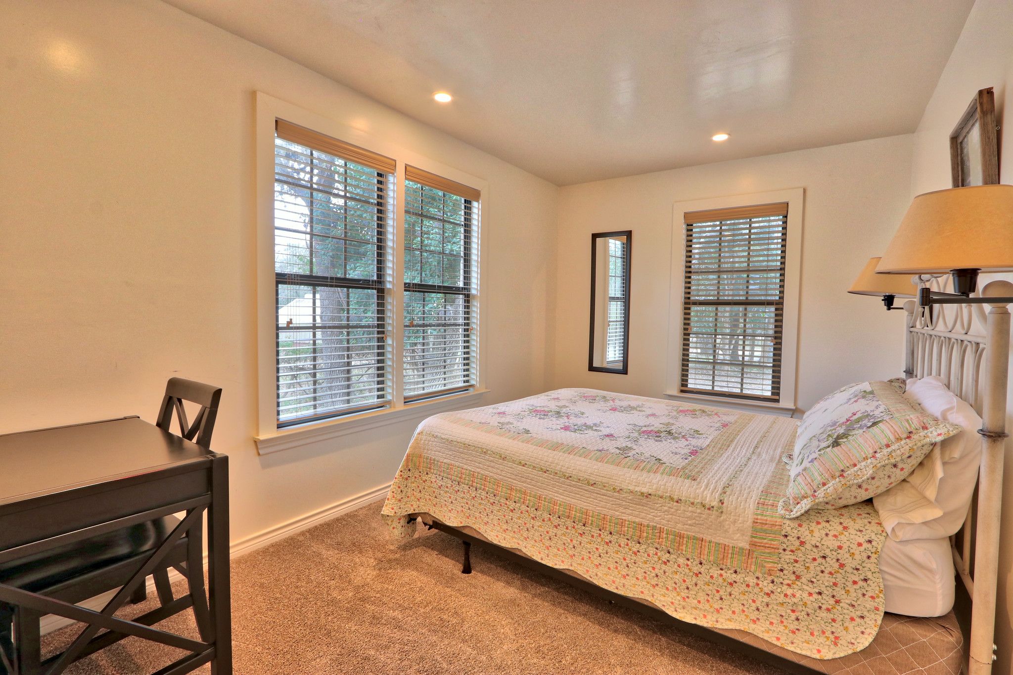 A bedroom with a bed, a desk, and two windows with blinds.