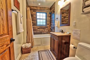 A bathroom with a wooden vanity, a bathtub, a window, and a shower curtain. - Caretaker's Cottage with Swimming Pool Access on a 75 Acre Ranch (Wimberley)