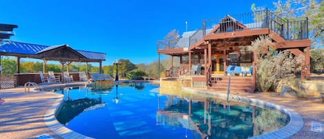 Zona de piscina con terraza de madera, sillas de descanso y un área de estar cubierta.