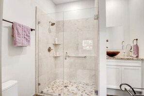 Un baño moderno con cabina de ducha de vidrio, tocador con espejo grande y retrete.