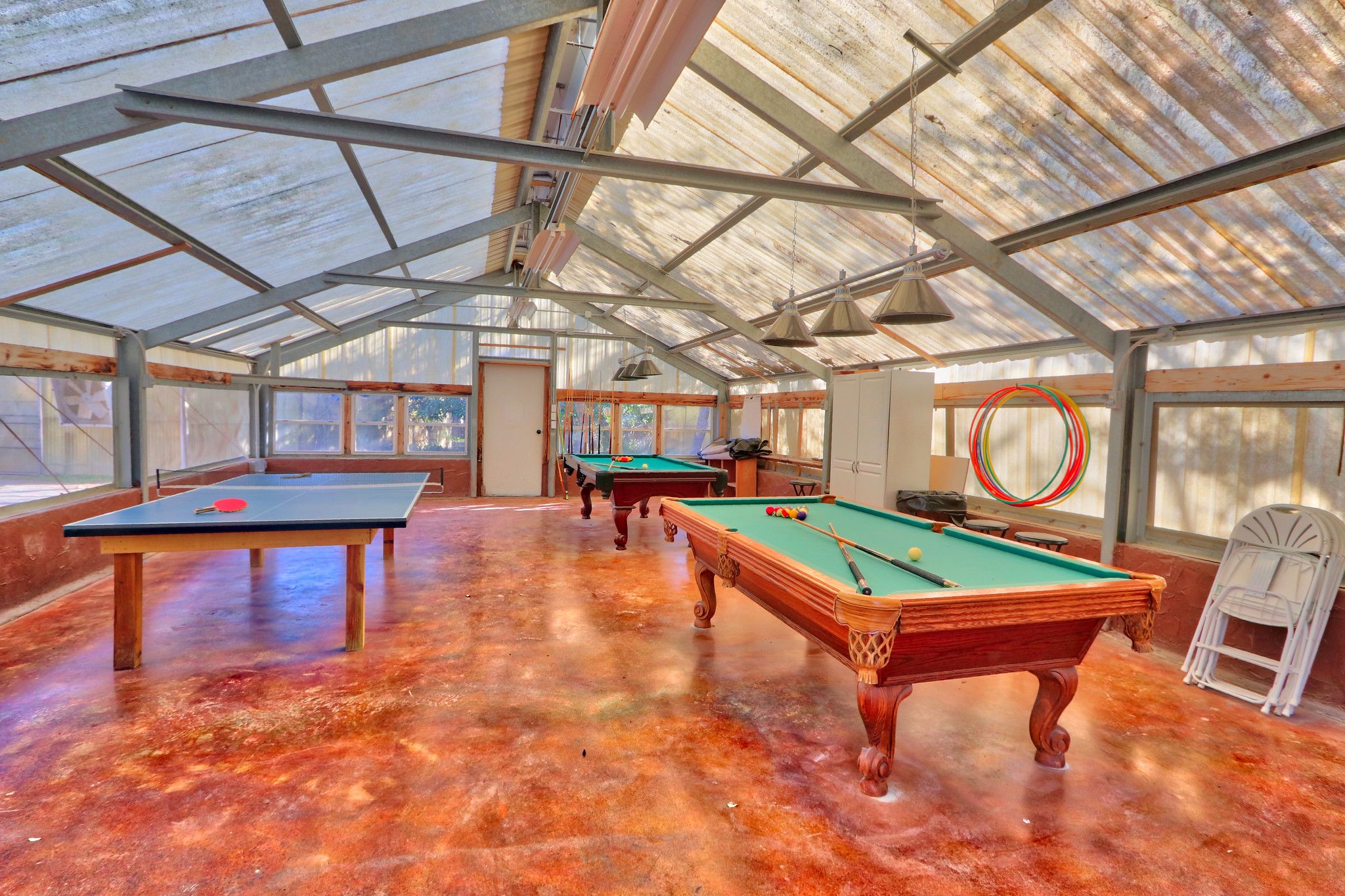 Amplia zona recreativa interior con varias mesas de billar y una mesa de ping pong, que cuenta con un techo alto con estructura metálica y grandes ventanales que permiten la entrada de luz natural.