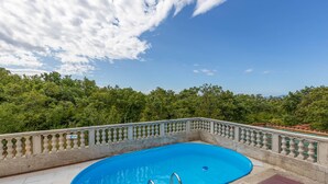 Una piscina con barandilla, rodeada de una solana con baldosas y vistas a un área boscosa.