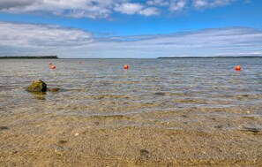 Una playa despejada con piedras, una roca y varios boyas anaranjadas en el agua.