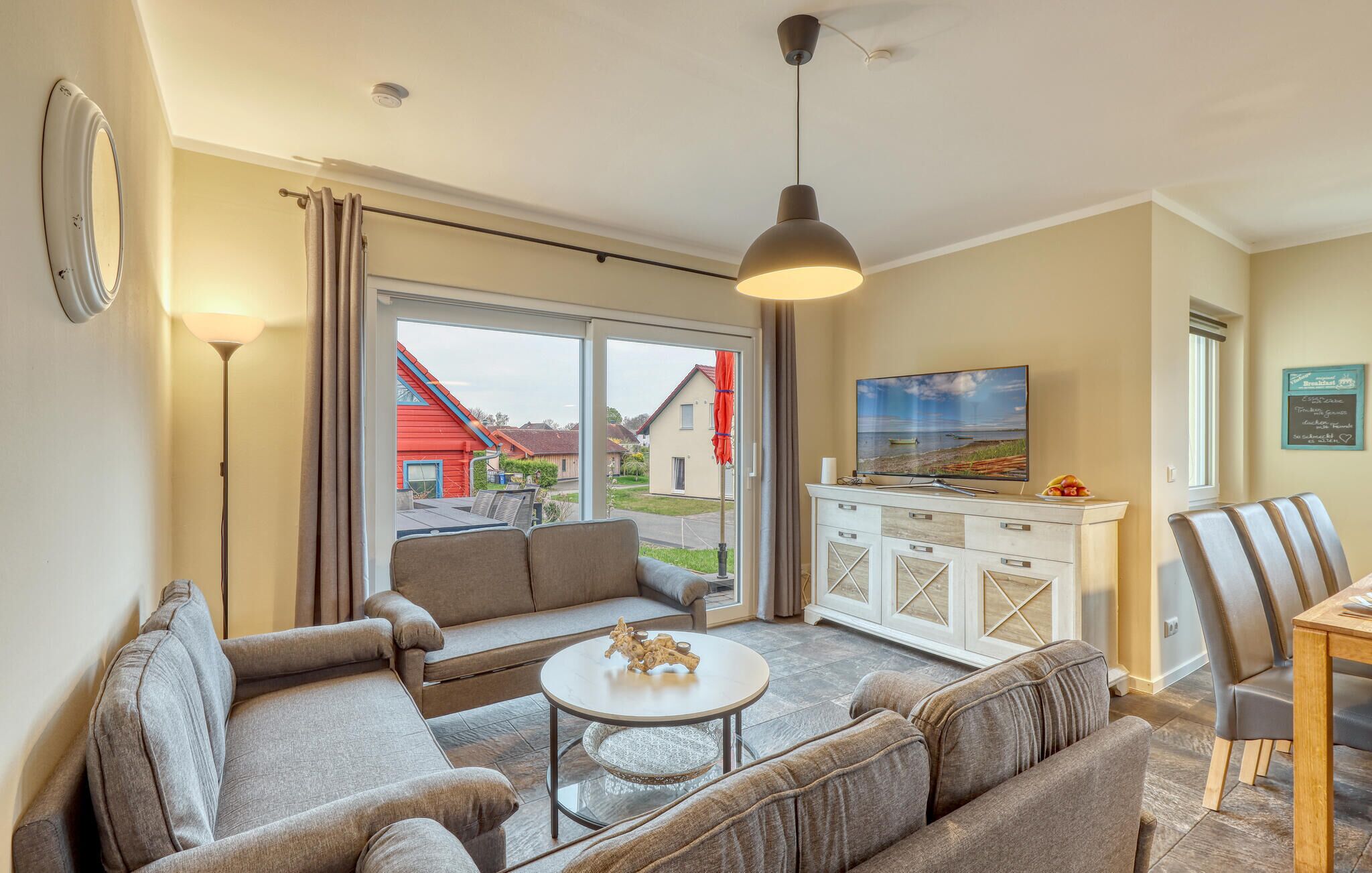 Ein Wohnzimmer mit einer Couch, einem Couchtisch, einem Fernseher und Blick auf ein rotes Haus durch die Glastür.