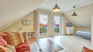 A loft bedroom with a sloped ceiling, a bed, a TV, a bookshelf, a clock, and a balcony with a view of houses. - 4 bedroom cozy home in Boiensdorf (Boiensdorf)