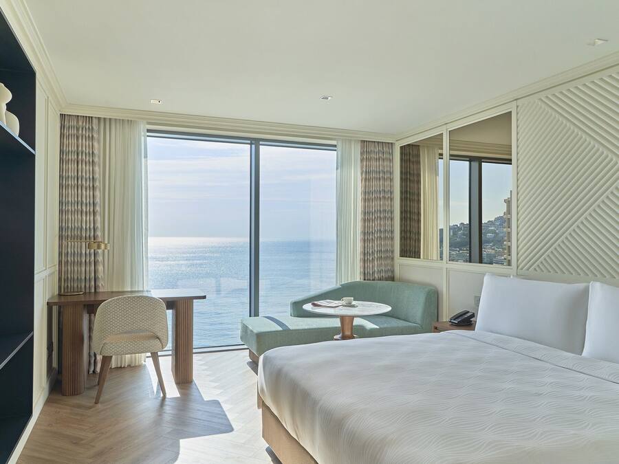 Habitación de hotel con una cama grande, zona de estar con una mesa y vista al mar.