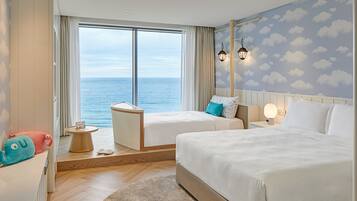 A hotel room with two beds, a view of the sea, a small table, and a nightstand with a lamp.