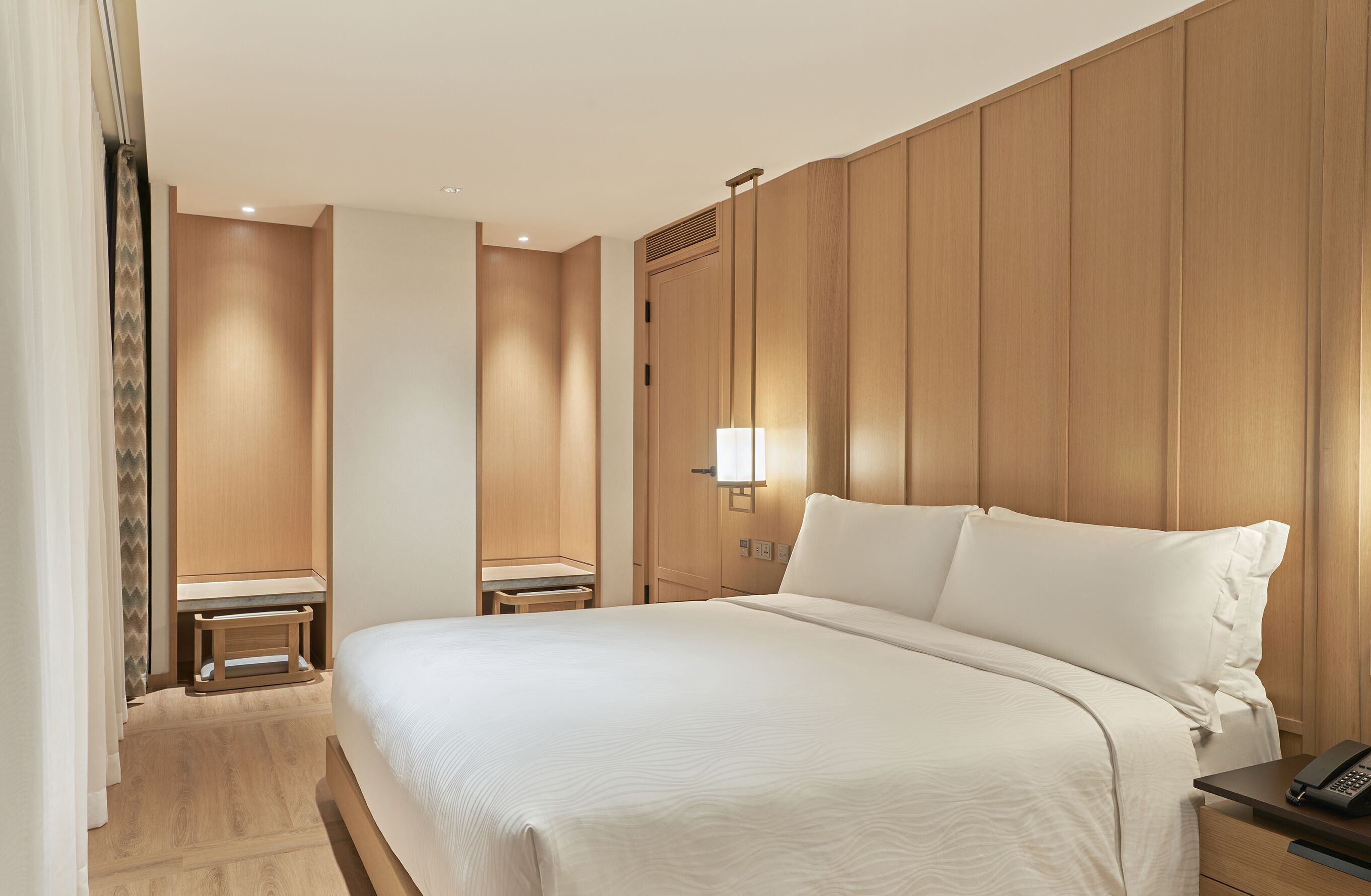A hotel room with a large bed, a bedside table with a lamp, and a wooden panel wall.