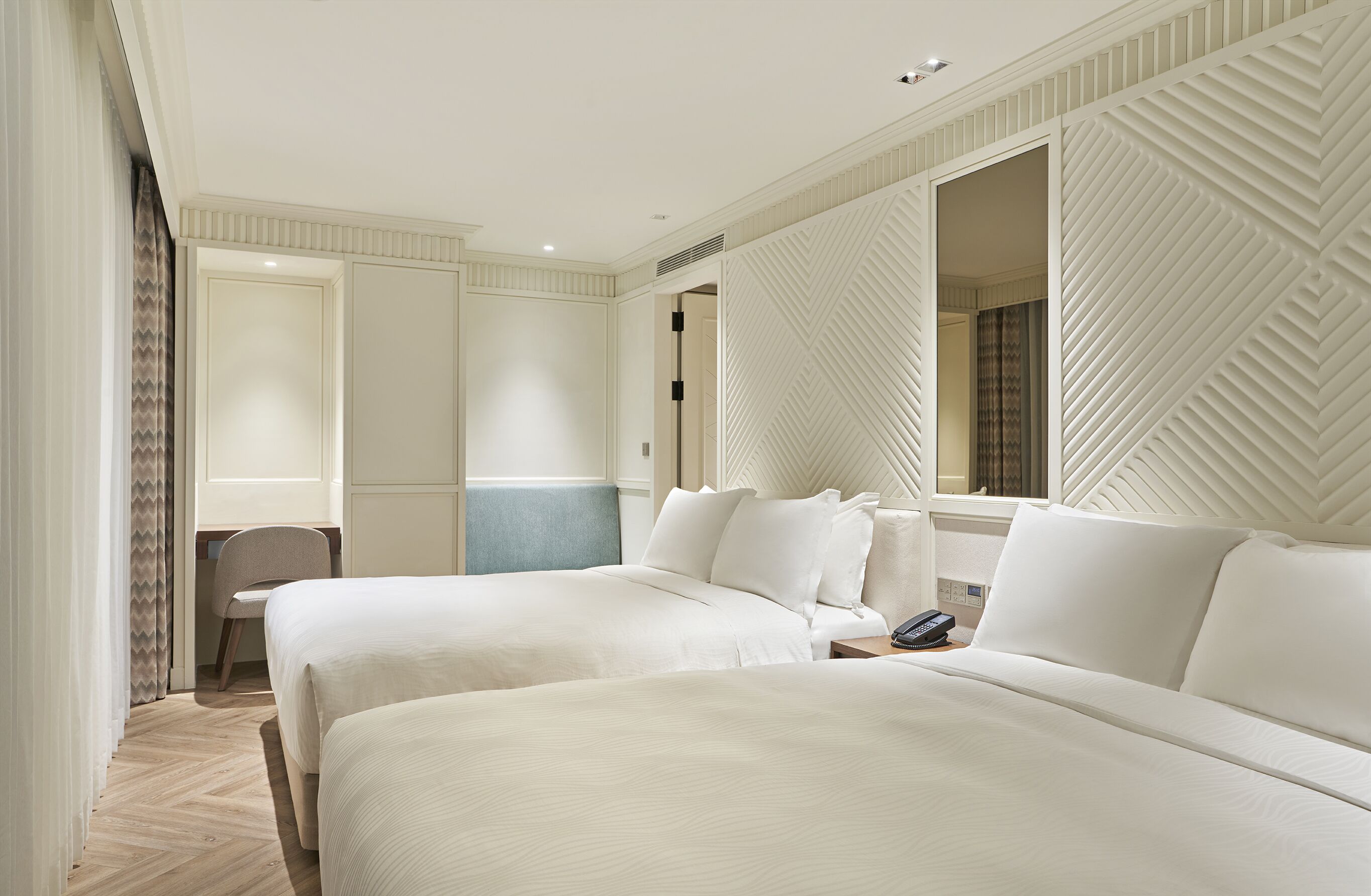 A hotel room with two beds, a desk, and a chair.