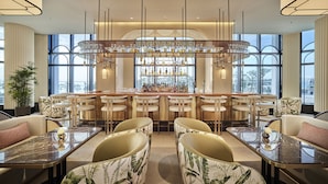 A modern bar area with a long counter, multiple bar stools, and a large chandelier. - Grand Josun Busan (Busan)