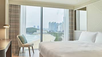Habitación de hotel con una cama grande, un escritorio y una silla. La habitación tiene vistas a la playa y al paisaje urbano.