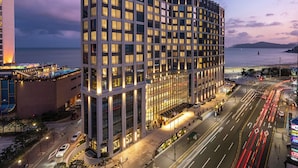 A modern hotel with multiple floors, a prominent entrance, and a view of the sea. - Grand Josun Busan (Busan)
