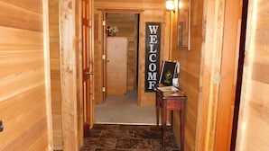 Un couloir en bois avec une pancarte indiquant « BIENVENUE », un bureau avec un ordinateur et une porte donnant sur une autre pièce.