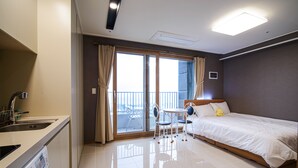 A hotel room with a bed, a small table with chairs, a sink, and a balcony with a view. - Sokcho Blue Terra Pension (Sokcho)