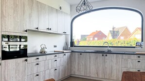 A modern kitchen with wooden cabinets, a black countertop, and a large window with a view of houses. - Amazing home in Diksmuide with WiFi (Diksmuide)