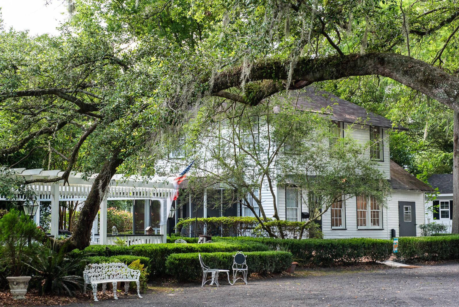 Una casa bianca con un portico, immersa nel verde e con un grande albero.