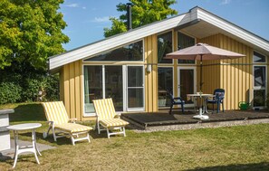 A yellow building with large windows, a patio with chairs and a table, and a covered area with an umbrella. - Beautiful home in Rechlin with sauna (Rechlin)