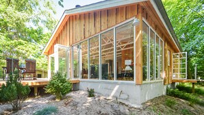 Une cabane moderne en bois, dotée de grandes fenêtres en verre, d’une terrasse et d’un jardin.