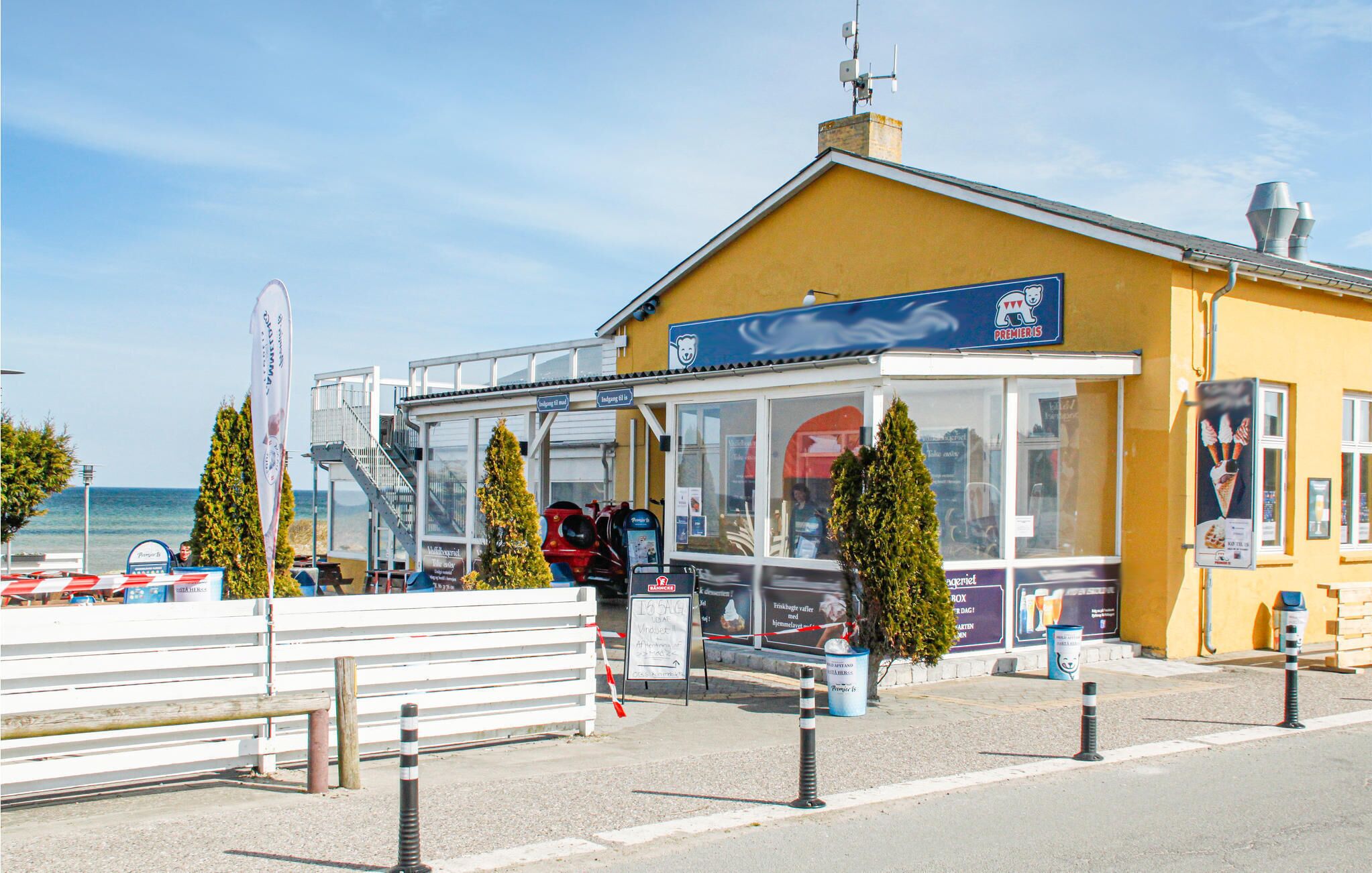 En gul byggnad med en blå skylt där det står ”Premieris”, och utsikt över havet.