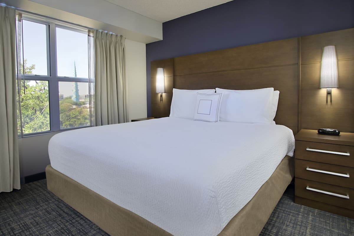 A hotel room with a large bed, a nightstand, two wall-mounted lamps, and a window with curtains.