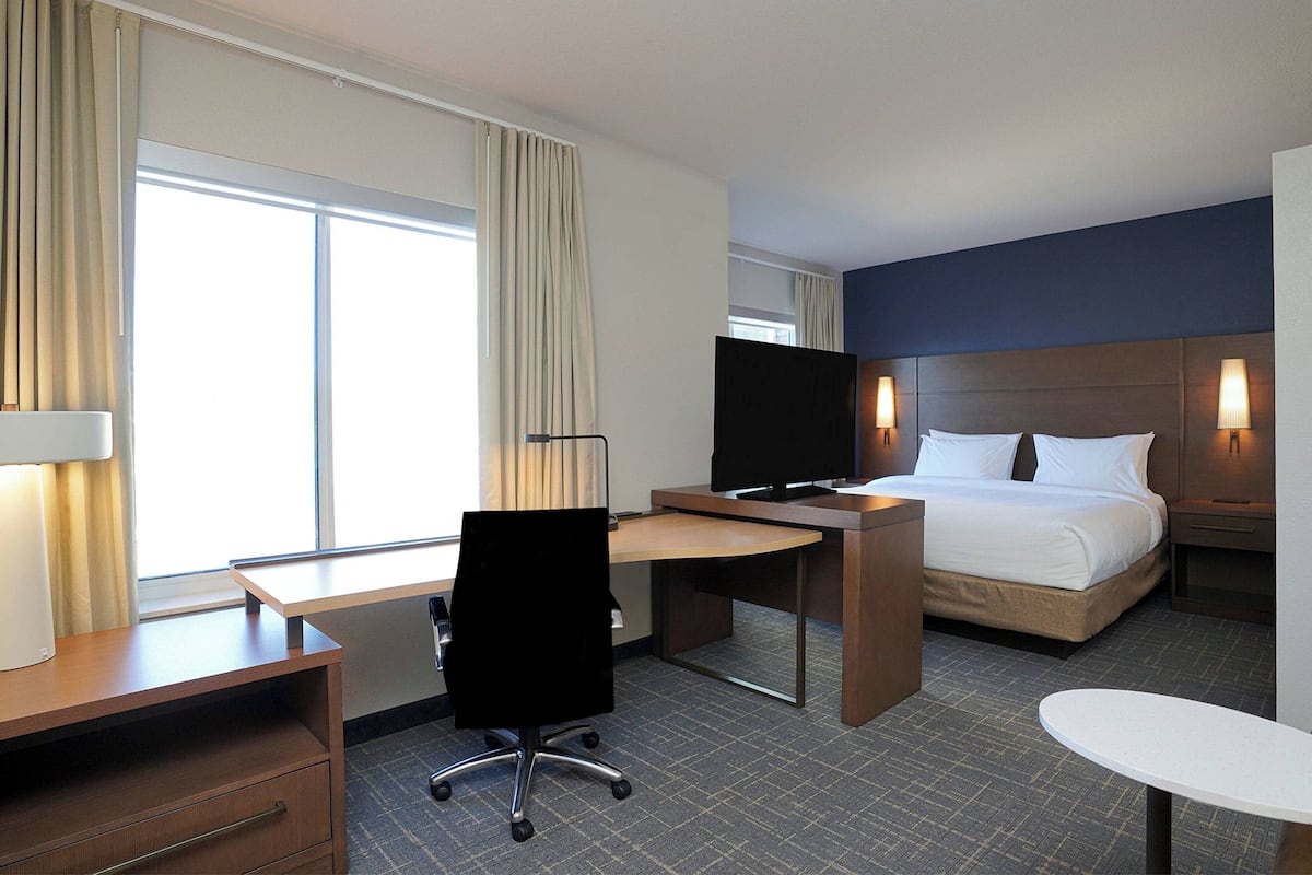 A hotel room with a bed, desk, chair, TV, and bedside lamps.