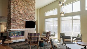 A spacious lobby with a brick fireplace, comfortable seating, large windows, and a modern chandelier.