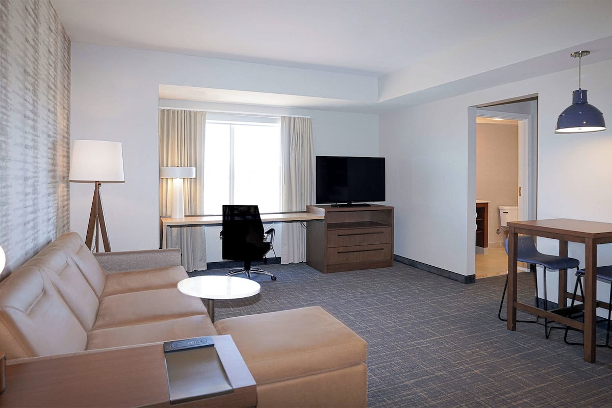 A hotel room with a sofa, a desk, a television, and a dining table.