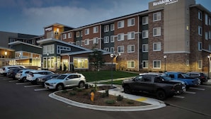 A multi-story hotel with a brick facade, a parking lot with several cars, and a well-lit entrance.