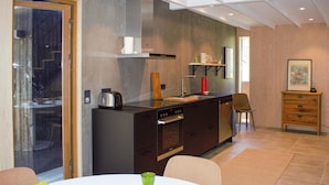 Een moderne keuken met donkere kastjes, een inbouwoven en een klein eiland met een spoelbak. Er is een eethoek met een tafel en stoelen, en een houten kast met lades.