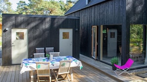 Een houten terras met een tafel, stoelen, een glazen deur en een kleine tuin.