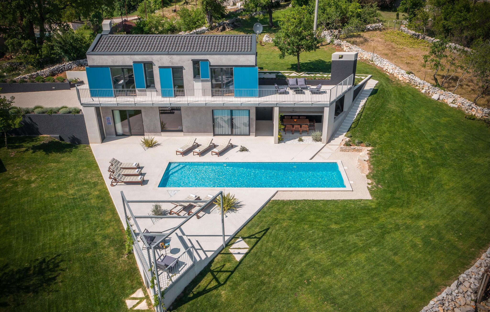 Ein modernes, zweistöckiges Haus mit Swimmingpool, Sitzgelegenheiten im Freien und einer Steinmauer.