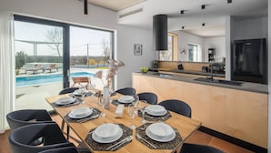 A modern dining area with a pool view, a kitchen with a large refrigerator, and a dining table set for six. - Beautiful home in Barban (Barban)