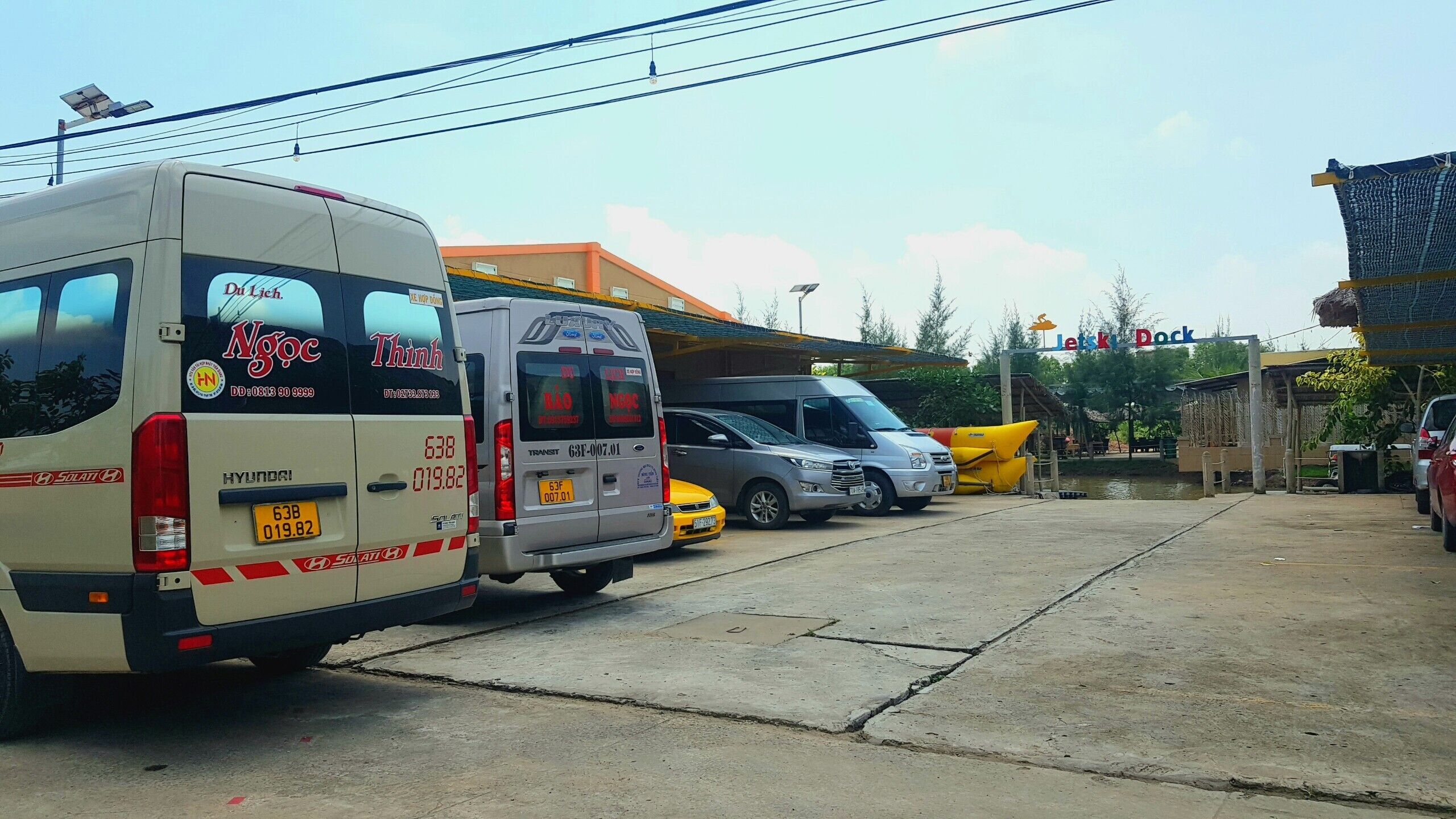 Un área de estacionamiento con varios vehículos, incluyendo una camioneta blanca y un auto plateado.