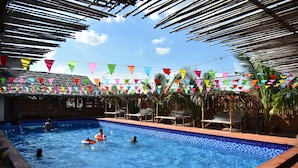 Une piscine dont les bords sont recouverts de carreaux, entourée de chaises longues et de parasols, et surmontée de drapeaux triangulaires aux couleurs vives.