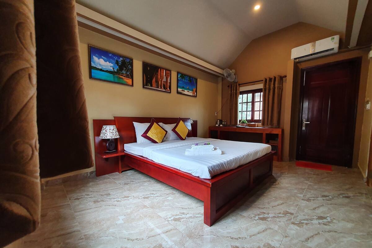 Een slaapkamer met een groot bed, een nachtkastje, een bureau en een raam met gordijnen.
