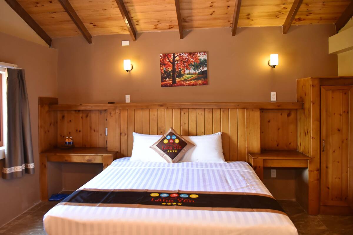 Een kamer met houten lambrisering, een bed, twee nachtkastjes, een raam met gordijnen en een aan de muur hangend schilderij.