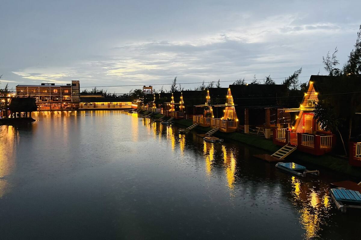 Een hotel aan de rivier met meerdere gebouwen, waaronder een groot gebouw met meerdere verdiepingen en kleinere gebouwen met balkons, verlicht door warme verlichting.