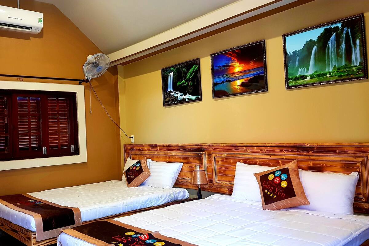 Een hotelkamer met twee bedden, een houten hoofdbord, een raam met luiken, wandgemonteerde airconditioning en drie ingelijste foto’s.