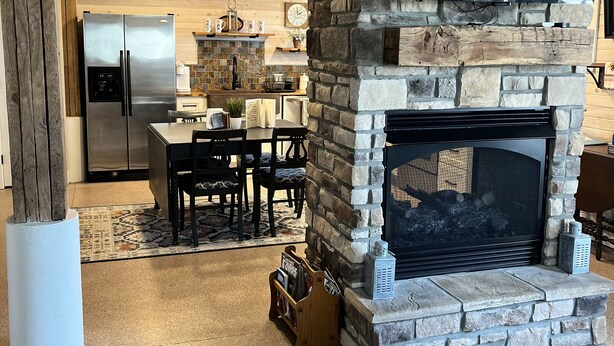 A cozy living room with a stone fireplace, a flat-screen TV mounted above it, and a modern kitchen in the background. - 2A2J Barn pool Getaway 9 miles to WEC (Wilmington)