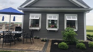 A house with a grey exterior, two windows with shutters, a patio with a table and chairs, and a blue umbrella. - 2A2J Barn pool Getaway 9 miles to WEC (Wilmington)