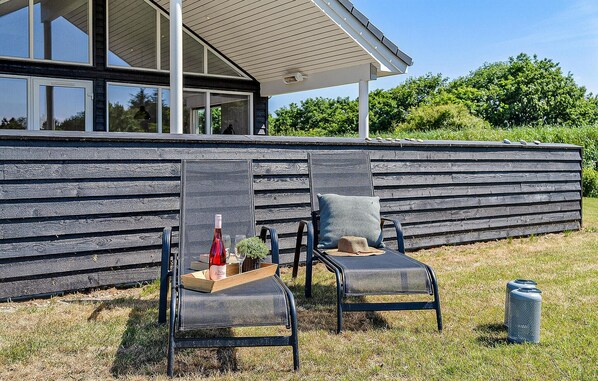 An outdoor seating area with two chairs and a table, a bottle of wine, and a glass.