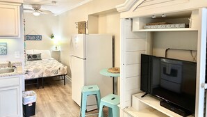 A compact living space with a kitchenette, a bed with a seashell-themed bedspread, a small dining area, and a television. - 2nd Floor Beachside Condo•Private Beach Access•Pool•Kitchen•Pet-Friendly (Atlantic Beach)