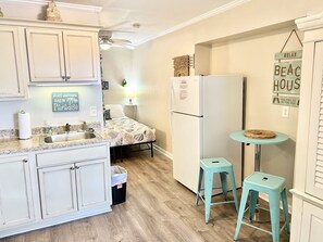 A compact kitchen with white cabinetry, a sink, a refrigerator, and a small dining area with a table and two stools. - 2nd Floor Beachside Condo•Private Beach Access•Pool•Kitchen•Pet-Friendly (Atlantic Beach)
