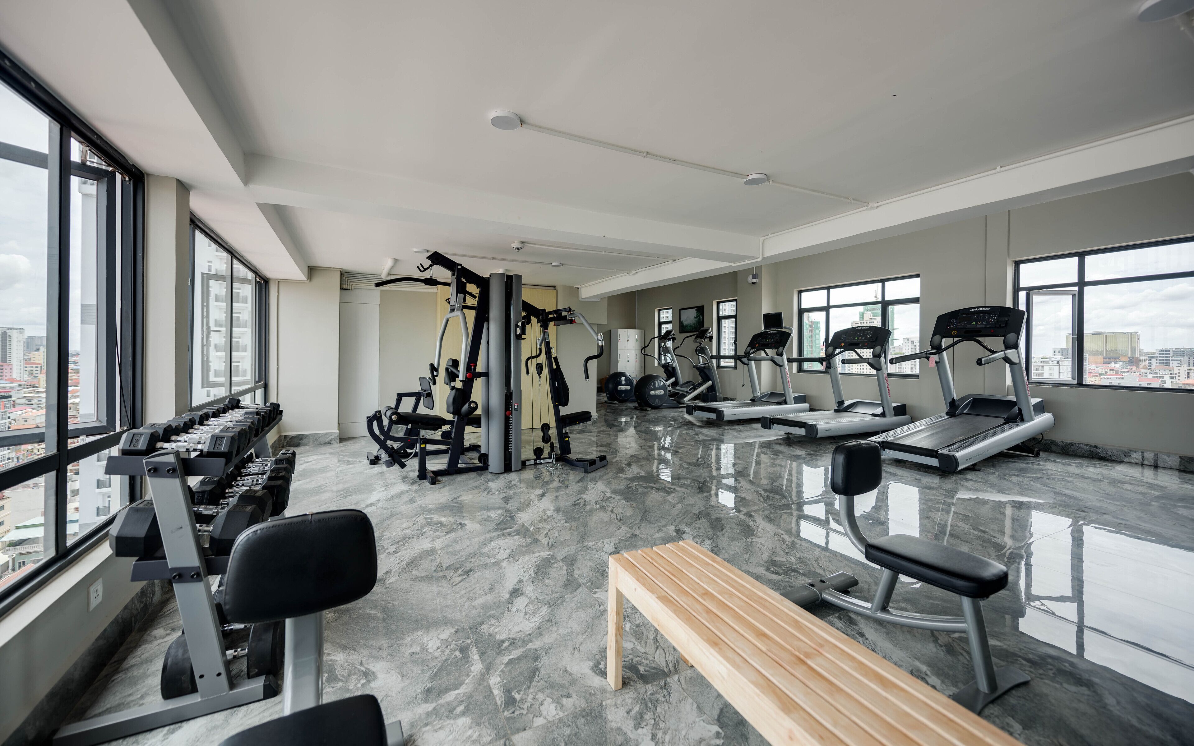 A modern gym with various exercise equipment, large windows, and a marble floor.