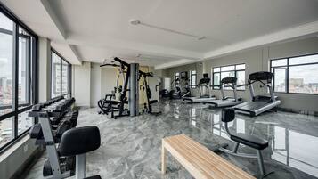 A modern gym with various exercise equipment, large windows, and a marble floor.
