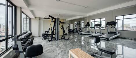 A modern gym with various exercise equipment, large windows, and a marble floor.