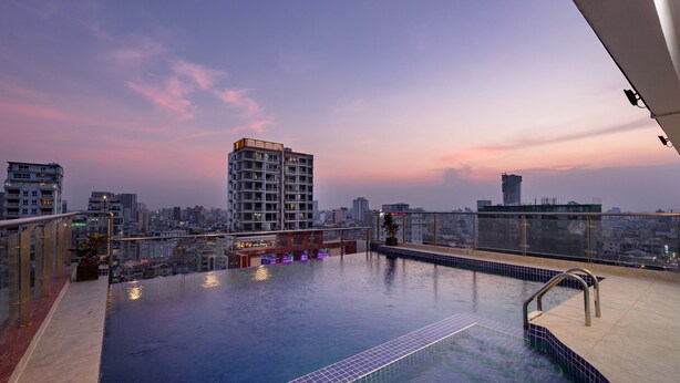 Una piscina infinita al aire libre con vistas a un horizonte urbano, barandilla de vidrio y zona de bar.