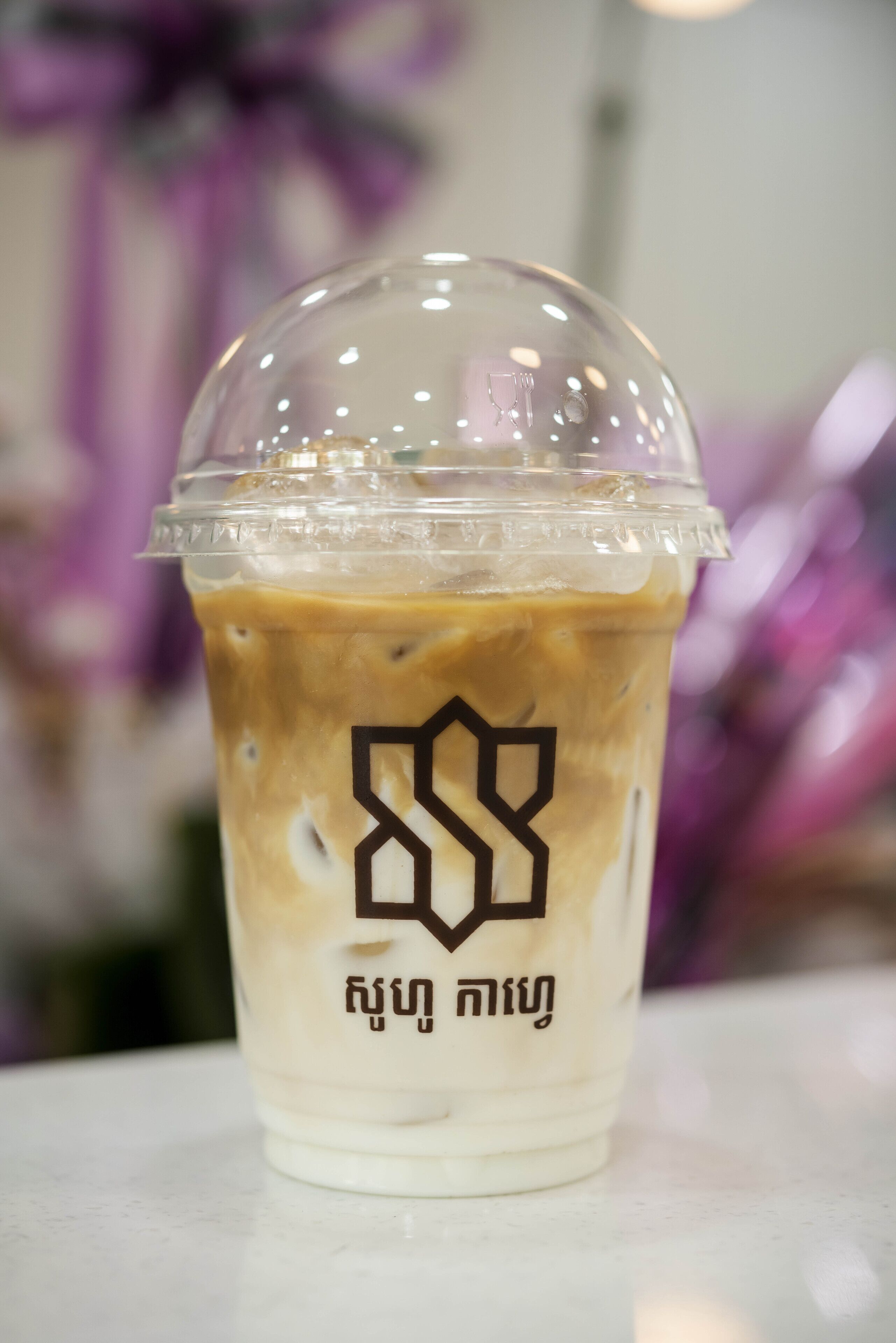 A clear plastic cup with a logo and text, containing a beverage.